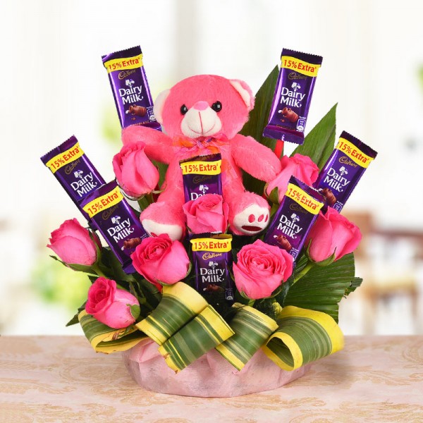 A Basket Arrangement of 8 Pink roses and 8 Cadbury's Dairy Milk of 13 gms each with Teddy bear (6 Inches) with dracaena leaves