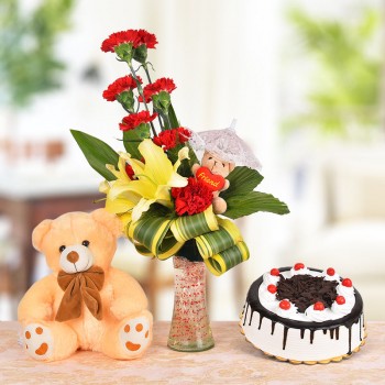 Floral Arrangement of 8 Red Carnations, 2 Yellow Asiatic Lilies and a 3 Inches Brown Teddy Bear with dracaena leaves in a Glass Vase a Brown Teddy Bear (12 Inches) and Half Kg Black Forest Cake