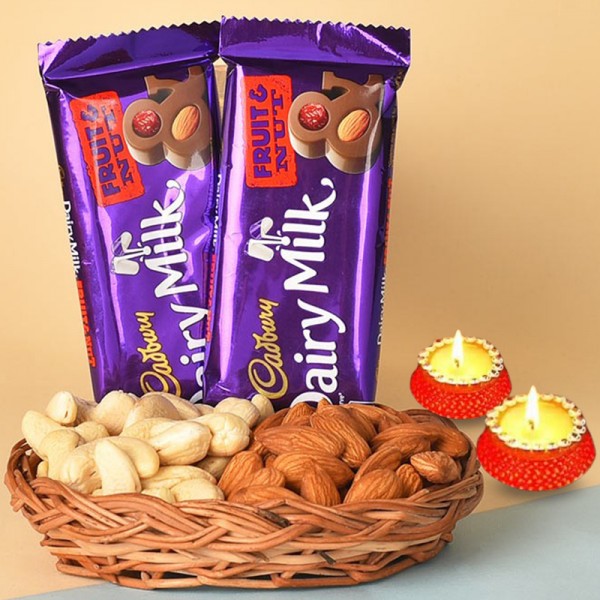 A Cane Basket containing Almonds (100 gms) and Cashew Nuts (100 gms) with 2 Cadbury Dairy Milk Fruit N Nut Chocolates (38 gms each) and Set of 2 Diya for Diwali